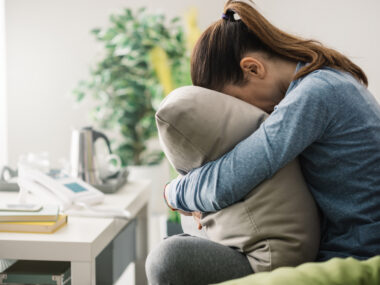 aggressive MS | MS News Today | Stock photo of a woman in a ponytail burying her face in a large pillow, to show struggle or difficulty.