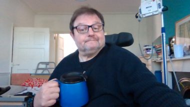 going out with MS | Multiple Sclerosis News Today | A photo shows John sitting in his wheelchair and holding a blue travel mug of coffee.