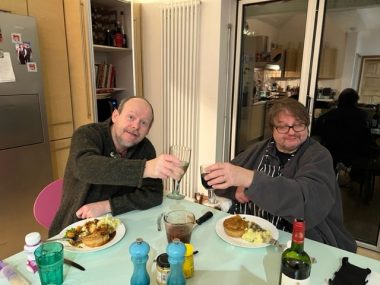 threes | Multiple Sclerosis News Today | two men at a table with food in front of them, both raising glasses of wine