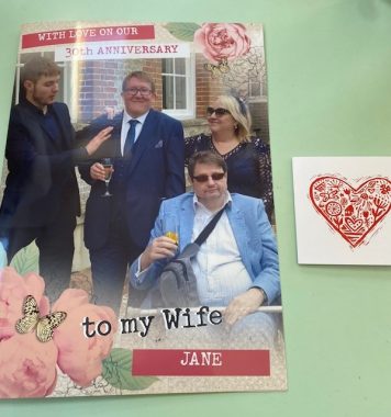 30th anniversary celebration | Multiple Sclerosis News Today | photo of anniversary card, with photos of John, his wife, and two others, reading, "With love on our 30th anniversary / to my Wife Jane." Beside it is a smaller card, with a heart on the cover