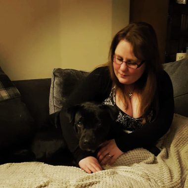 benefits of pets | Multiple Sclerosis News Today | Beth lies on the couch with her black Staffordshire terrier, Ivy.