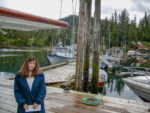 Melissa Cook stands on a dock under the wing of a small airplane in front of boats.