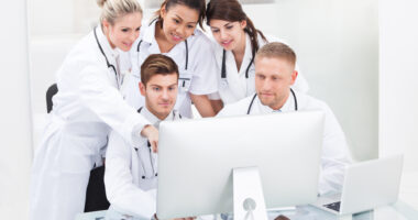 A team of healthcare specialists in white coats conferring around a computer.