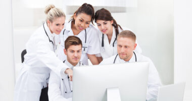 A team of healthcare specialists in white coats conferring around a computer.