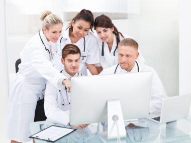A team of healthcare specialists in white coats conferring around a computer.