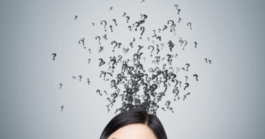 A woman looking up at question marks above her head on a gray background