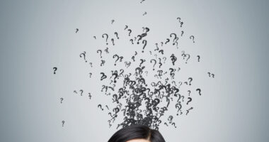 A woman looking up at question marks above her head on a gray background