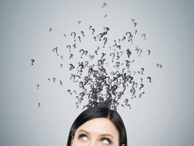 A woman looking up at question marks above her head on a gray background