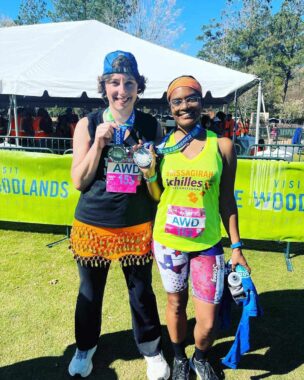 Two women pose with medals after running a half marathon.