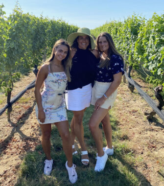 Mother and two daughters pose together in a sunny vineyard. 
