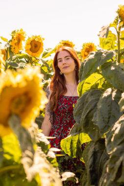A woman stands in a field of sunflowers taller than her. 