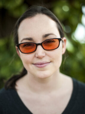 A headshot features a woman wearing glasses with orange lenses. 