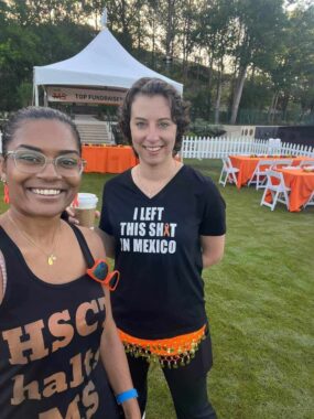 Two women pose for a photo at an MS event. One wears a tank top that says "HSCT halts MS" and the other wears a T-shirt that says "I left this s*** in Mexico," and the letter "I" in the S-word has been replaced with an orange awareness ribbon.