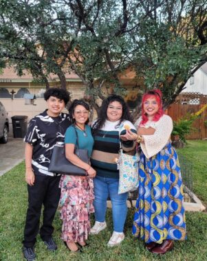 Four people stand outside in front of a tree, in what appears to be someone's front yard. The author is on the far right, and her brother is on the far left. In between them are their mom and aunt. They're all dressed nicely, with two of the women wearing long colorful skirts.