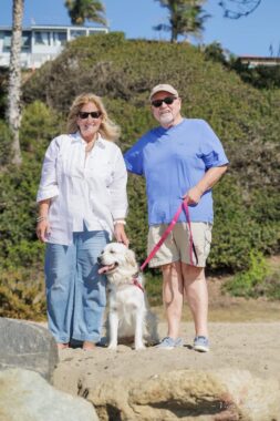 A woman and a man, Jenn and Mike Powell, stand on a rock with a dog.
