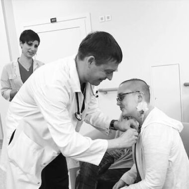 A black-and-white photo shows a doctor affixing an iris pin to a woman's shirt on the day of her stem cell transplant.