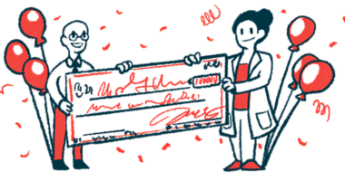 Two people, one in a white coat, hold an oversized check flanked by balloons.