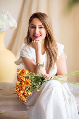 Sanam Saeedi rests her hand in her chin and holds a bouquet of flowers.