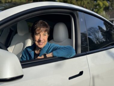 A woman is shown in her car, with the window down, smiling. 