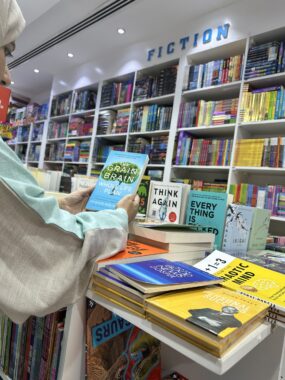 A woman is just visible to the left, only partly visible in the photo. She's standing in a bookstore next to a table and holding up a book titled "The Grain Brain Whole Life Plan."