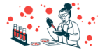 A scientist works with a petri dish in a lab, alongside a rack of four vials filled with liquid.