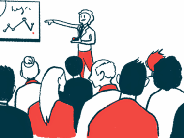 A conference presenter points to a white board while speaking to a large audience.