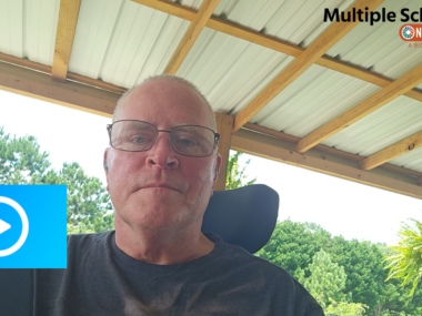 A man in a wheelchair looks into a video camera to record a video.