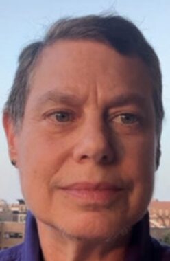 A close-up photo shows a woman smiling softly and looking just to the right of the camera. We can't see much of the background, but she is standing outside under a clear blue sky.