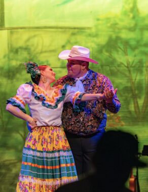 A man and a woman, both dressed in traditional Mexican outfits, dance onstage as a duet.