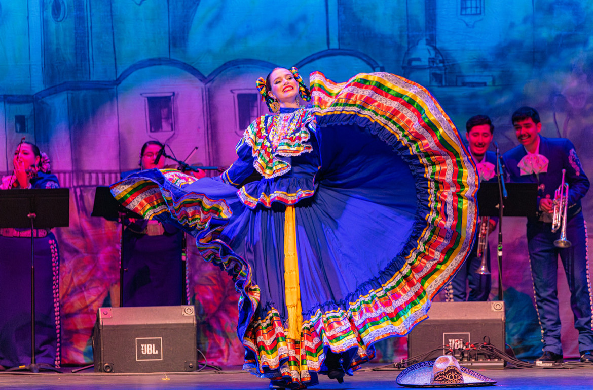 A woman wearing a traditional Mexican dress performs a dance onstage.