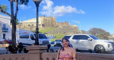 A woman sits on a bench outside next to a busy street in Puerto Rico.