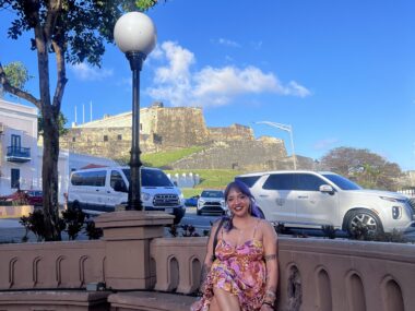 A woman sits on a bench outside next to a busy street in Puerto Rico.