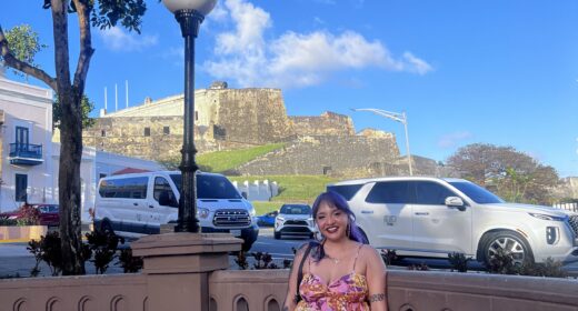 A woman sits on a bench outside next to a busy street in Puerto Rico.