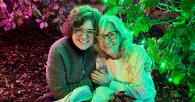 A woman and her grandmother embrace each other in a garden with some trippy pinkish-red and green lights casting a dynamic glow over the two's faces.