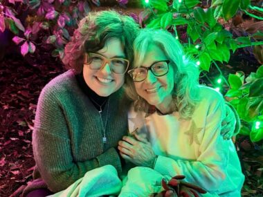 A woman and her grandmother embrace each other in a garden with some trippy pinkish-red and green lights casting a dynamic glow over the two's faces.