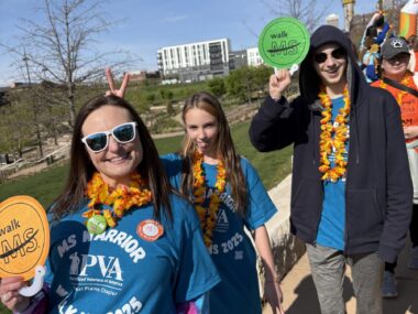 A mother, young daughter and young son, pose on a sunny day during an advocacy event. They're all wearing blue MS advocacy T-shirts and colorful lei.