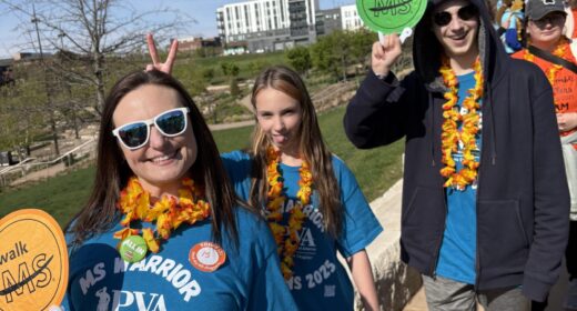 A mother, young daughter and young son, pose on a sunny day during an advocacy event. They're all wearing blue MS advocacy T-shirts and colorful lei.