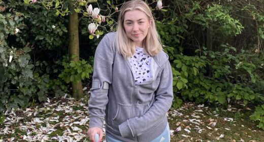 A young woman with blond hair is pictured in her garden, leaning on a cane.