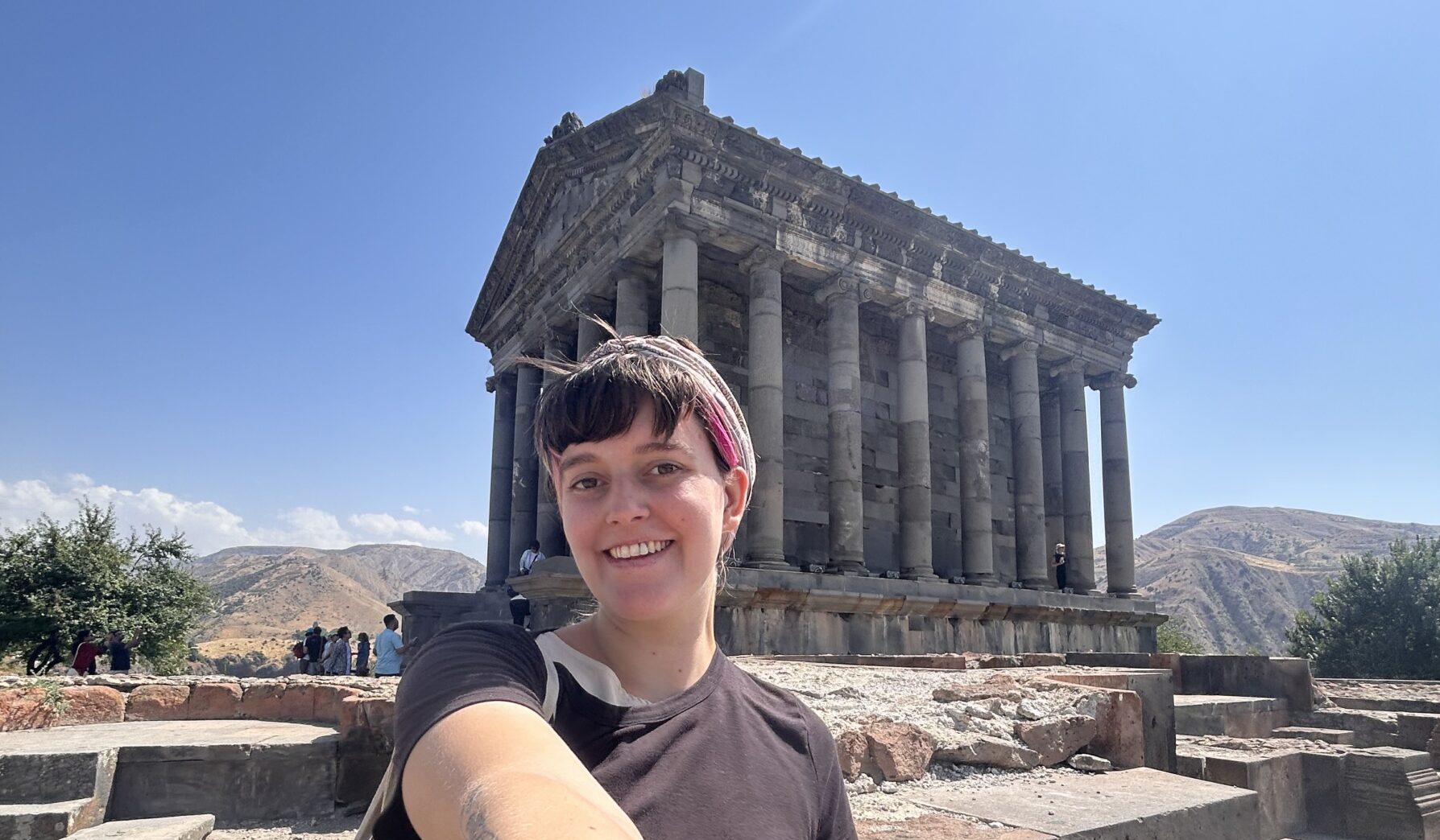 A woman takes a selfie in front of an ancient unidentified structure outdoors, probably somewhere in Europe, likely Greece.