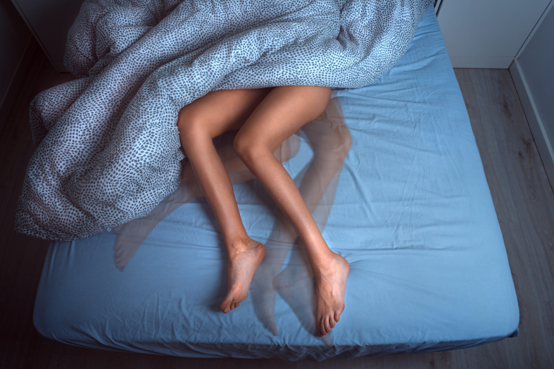 A person lies in bed, with their legs uncovered and more faint images showing the legs in different positions.