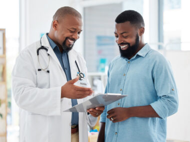 A doctor gestures at a clipboard while showing a patient his records.