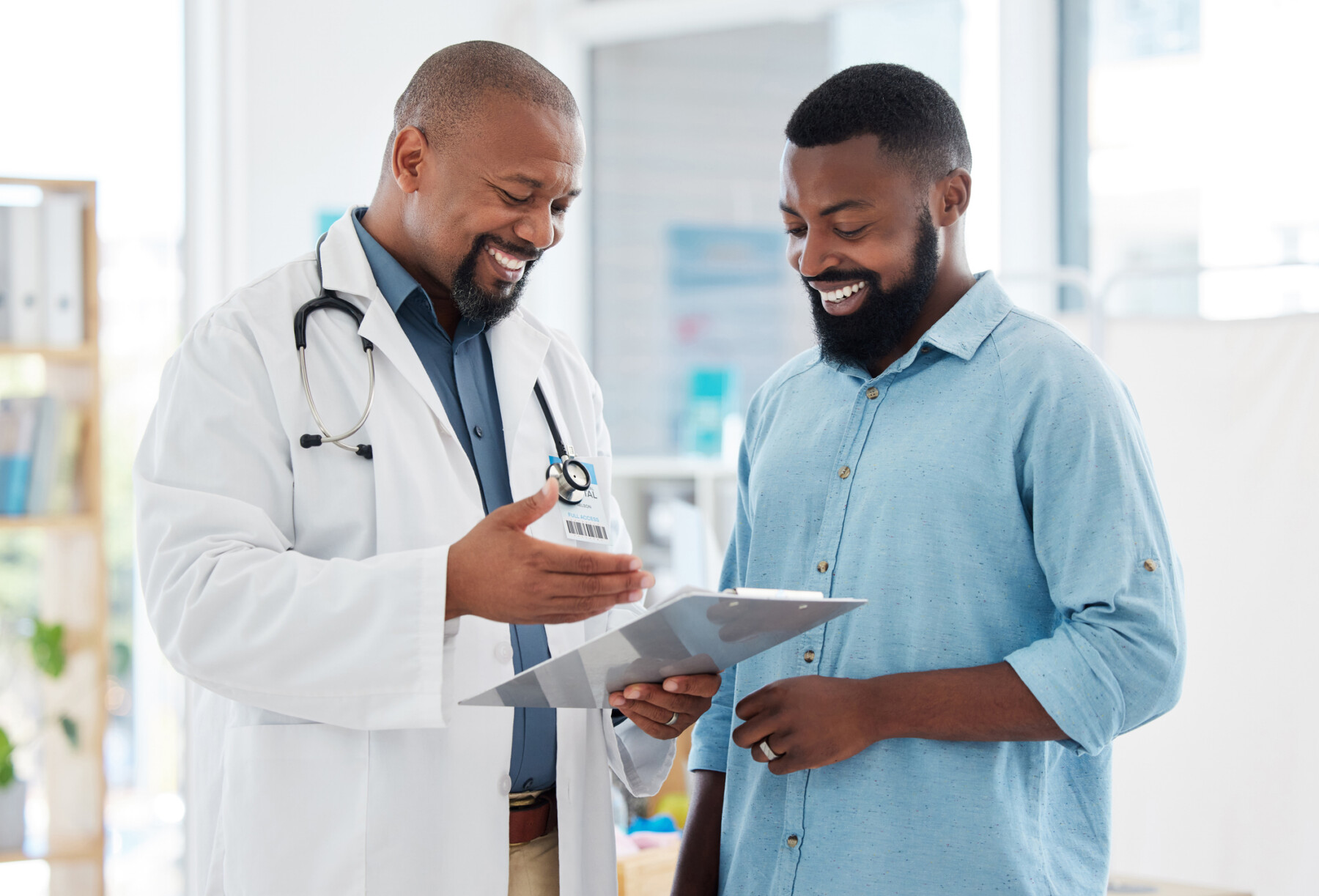 A doctor gestures at a clipboard while showing a patient his records.