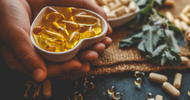 A hand holds vitamin D softgel capsules, representing vitamin D supplementation studied for MS relapse risk.