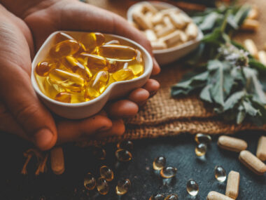 A hand holds vitamin D softgel capsules, representing vitamin D supplementation studied for MS relapse risk.