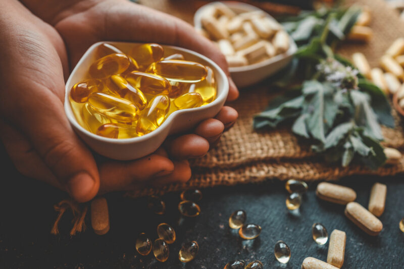 A hand holds vitamin D softgel capsules, representing vitamin D supplementation studied for MS relapse risk.