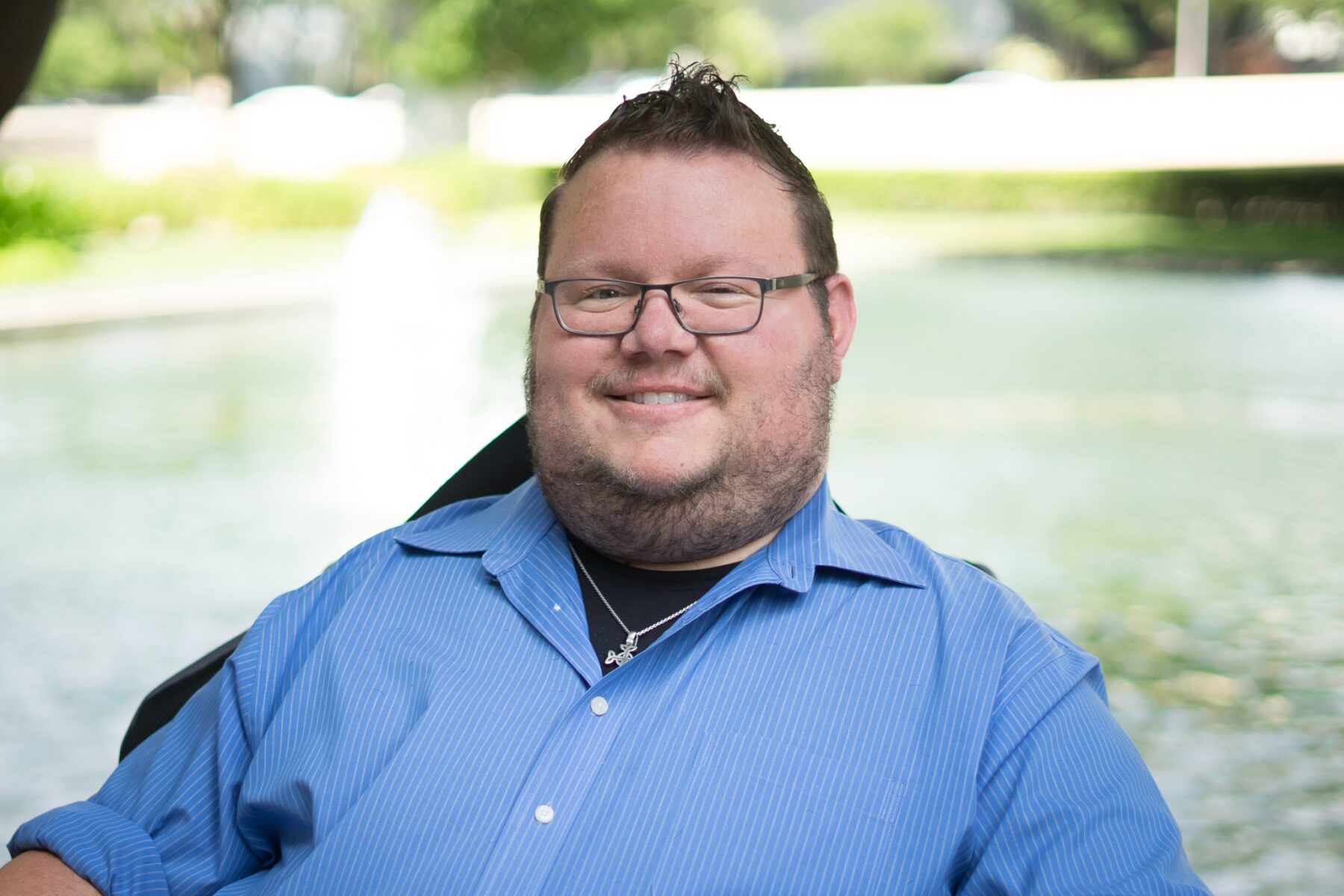 A pretty tight horizontal profile pic of a man in a blue dress shirt, short-cropped hair, and glasses, smiling broadly.