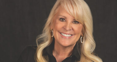A headshot features a woman with blond hair smiling against a dark background.