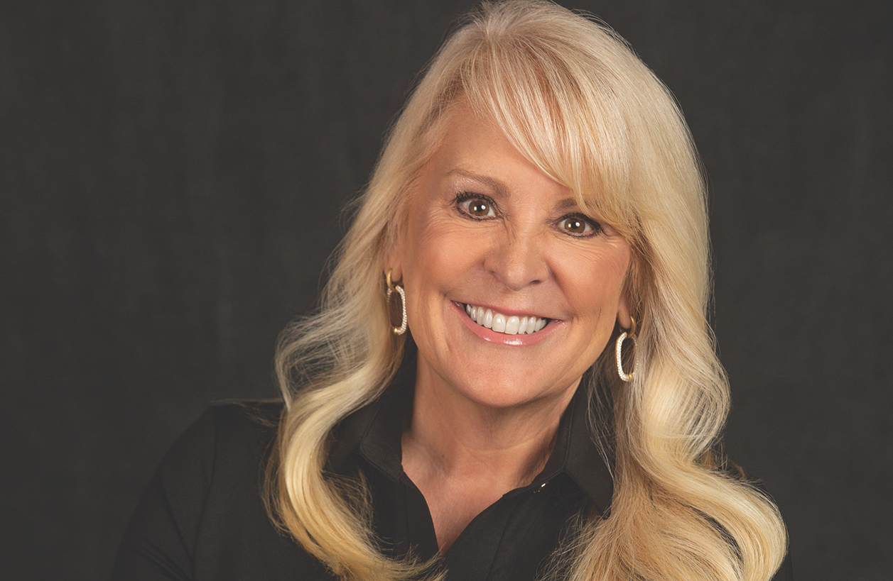 A headshot features a woman with blond hair smiling against a dark background.