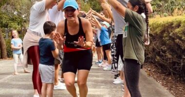 A woman in a baseball cap is seen coming out of the end of a human tunnel made by people clasping their hands together overhead.
