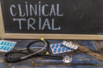 A stethoscope and oral medication packets are seen in front of a blackboard with the words 